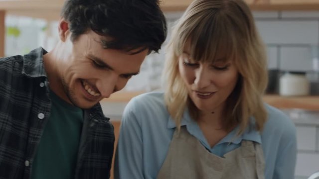 happy couple cooking in kitchen young man chopping vegetables with sneaky girlfriend stealing carrots smiling playfully enjoying fun preparing dinner together at home 4k footage