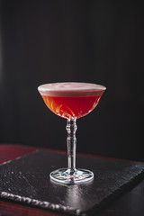Clover Club Cocktail with Gin, Lemon Juice, Raspberries, and Egg White Foam in a Glass in a Dark Luxurious Bar