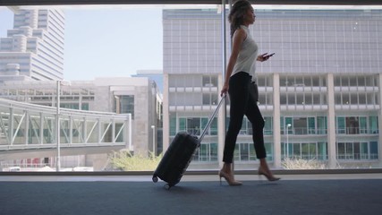young business woman traveler walking using smartphone pulling trolly bag in airport texting checking messages female commuter traveling international for business trip 4k - Powered by Adobe