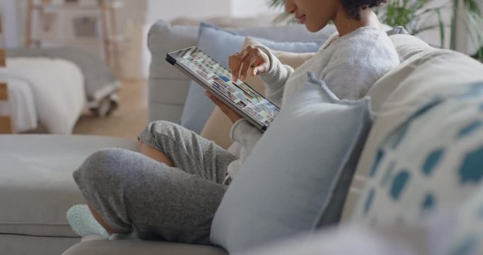 young woman browsing online using tablet computer scrolling looking at social media pictures with mobile touchscreen technology relaxing on sofa at home 4k