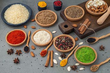 Spices lie in bowls and wooden spoons on a gray background , top view, soft focus. Spices and seasonings for cooking in the composition on the table.