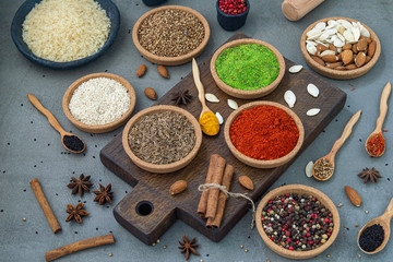 Spices lie in bowls and wooden spoons on a gray background , top view, soft focus. Spices and seasonings for cooking in the composition on the table.