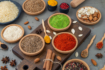 Spices lie in bowls and wooden spoons on a gray background , top view, soft focus. Spices and seasonings for cooking in the composition on the table.