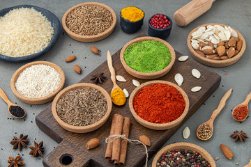 Spices lie in bowls and wooden spoons on a gray background , top view, soft focus. Spices and seasonings for cooking in the composition on the table.