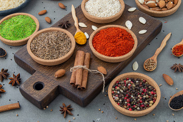 Spices lie in bowls and wooden spoons on a gray background , top view, soft focus. Spices and seasonings for cooking in the composition on the table.
