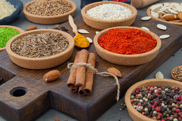 Spices lie in bowls and wooden spoons on a gray background , top view, soft focus. Spices and seasonings for cooking in the composition on the table.