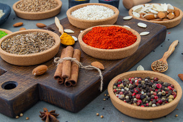 Spices lie in bowls and wooden spoons on a gray background , top view, soft focus. Spices and seasonings for cooking in the composition on the table.