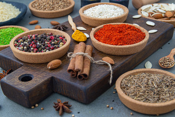 Spices lie in bowls and wooden spoons on a gray background , top view, soft focus. Spices and seasonings for cooking in the composition on the table.
