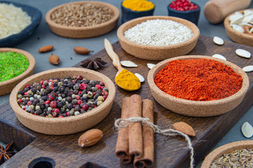 Spices lie in bowls and wooden spoons on a gray background , top view, soft focus. Spices and seasonings for cooking in the composition on the table.