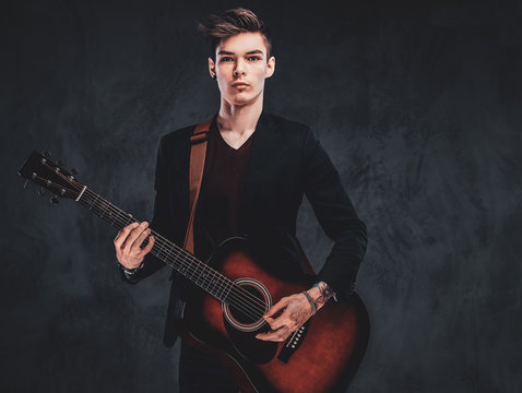 Young attractive man is playing acoustic guitar at studio while posing for photographer.