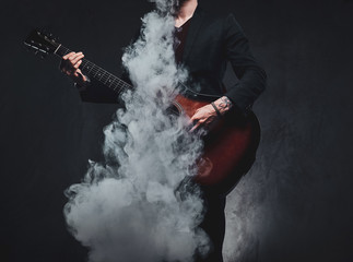 Obraz premium Młody atrakcyjny mężczyzna gra na gitarze akustycznej podczas palenia vape, robiąc wielką mgiełkę.