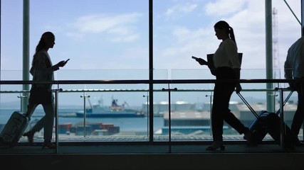 business people at busy airport pulling trolley bags arriving and departing terminal tourists travelling international walking in lobby with view of harbor port 4k footage - Powered by Adobe