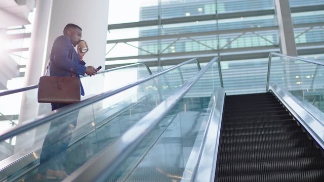 young african american businessman using smartphone on escalator texting drinking coffee checking email messages successful male executive arriving at work in corporate office building 4k