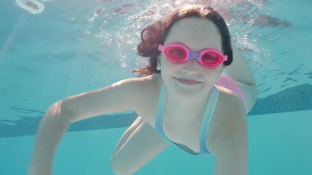 happy girl swimming underwater in pool smiling waving hand enjoying swim in crystal clear water wearing goggles enjoying summer 4k