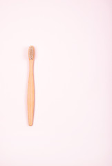 Top view of bamboo toothbrush on pastel pink background. Plastic free concept.