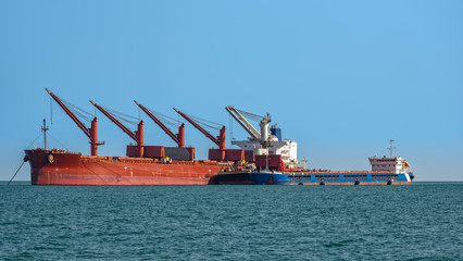 Loading ocean-going bulk carrier ship with Bauxite aluminum ore from the mini bulk carrier (feeder) vessel at offshore Kamsar port, Guinea, West Africa.