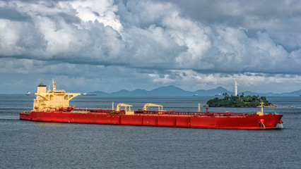 Laden crude oil tanker passes the Strait of Singapore in front of island with white lighthouse.