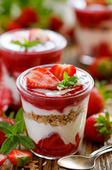 Strawberry layered dessert, healthy dessert with fresh strawberries, natural yoghurt, strawberry mousse and granola in glass dishes on a wooden table. Delicious and nutritious dessert or breakfast