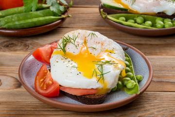 Close up view of poached egg with onion and peas and tomato on a plate. Wooden background. Soft focus