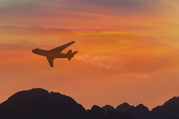 Fototapeta na wymiar travel concept background, airplane silhouette in sunset sky, international flight over mountains