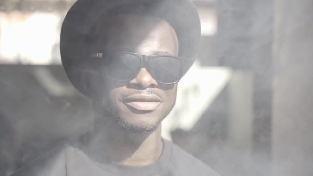 African man with hat and sunglasses vaping tobacco.