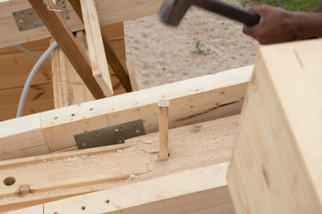 Workers, carpenters, hammering wooden pins with a sledgehammer. Details of a wooden house. The beams of the ceiling and the walls of the house of glued laminated timber. Summer day.