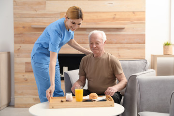 Nurse serving breakfast to elderly man indoors. Assisting senior people - Powered by Adobe