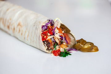 Shawarma sandwich - fresh roll of thin lavash (pita bread) filled with grilled meat, mushrooms, cheese, cabbage, carrots, sauce, green. Traditional Eastern snack. On a wooden background