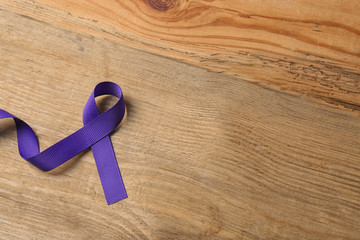 Purple ribbon on brown wooden background, space for text. Domestic violence awareness