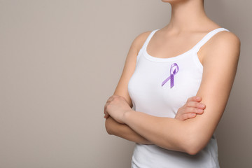 Woman wearing purple ribbon on grey background, closeup with space for text. Domestic violence...