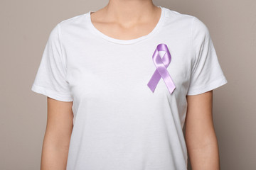 Woman wearing purple ribbon on grey background, closeup. Domestic violence awareness