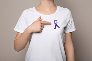Woman wearing purple ribbon on grey background, closeup. Domestic violence awareness