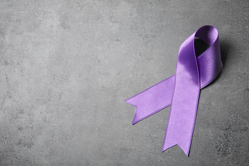 Purple ribbon on grey stone background, space for text. Domestic violence awareness