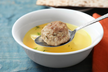 Spoon with matzoh ball over bowl of soup on table, closeup. Jewish cuisine