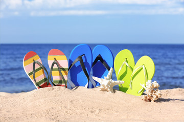 Fototapeta na wymiar Composition with bright flip flops on sand near sea in summer. Beach accessories