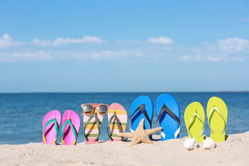 Fototapeta na wymiar Composition with bright flip flops on sand near sea in summer. Beach accessories