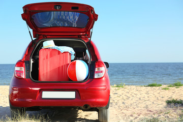 Suitcase and beach accessories in car trunk on sand near sea. Space for text