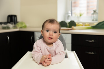 Fototapeta premium The baby is sitting at the children's chair and waiting for her mother to feed her. Child plays.