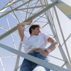 Young girl with a stylish short hair against the blue sky and a telecommunication iron tower....