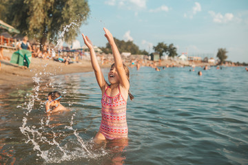 Beautiful little girl having fun in water, her hands splashing sea water