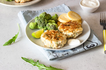 Delicious cutlets (fish or meat) with broccoli, potatoes and sauce on a plate. Light grey stone background. 