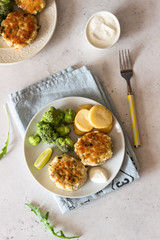 Delicious cutlets (fish or meat) with broccoli, potatoes and sauce on a plate. Light grey stone background. 
