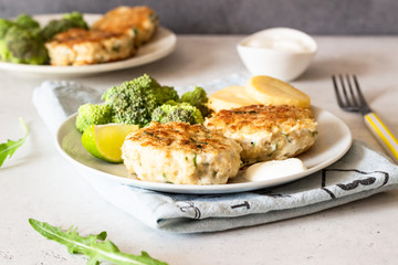 Delicious cutlets (fish or meat) with broccoli, potatoes and sauce on a plate. Light grey stone background. 