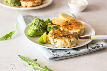 Delicious cutlets (fish or meat) with broccoli, potatoes and sauce on a plate. Light grey stone background. 