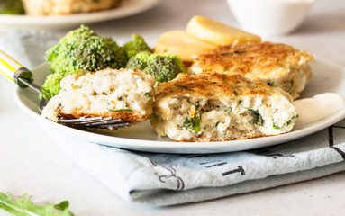 Delicious cutlets (fish or meat) with broccoli, potatoes and sauce on a plate. Light grey stone background. 