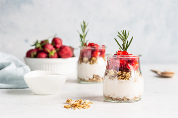 Breakfast with yogurt, granola and fresh strawberry in a mason jar on a light stone background. Healthy breakfast or dessert concept, selective focus. Copy space.