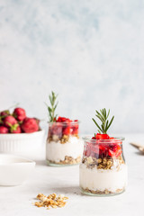 Fototapeta na wymiar Breakfast with yogurt, granola and fresh strawberry in a mason jar on a light stone background. Healthy breakfast or dessert concept, selective focus. Copy space.