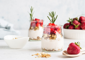 Breakfast with yogurt, granola and fresh strawberry in a mason jar on a light stone background. Healthy breakfast or dessert concept, selective focus. Copy space.