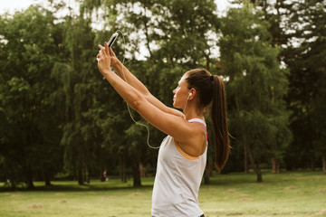  Beautiful fitness girl, phone and headphones. Training in nature