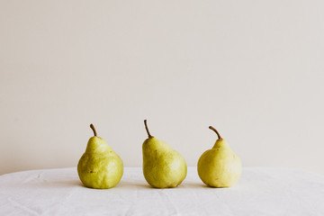 Closeup of three pears on white tablecloth against neutral wall background